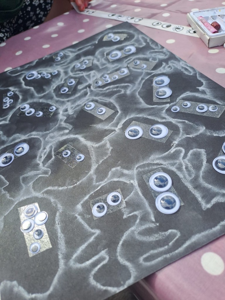 Photo of black card, covered in googly eyes to make an army of small cute creatures