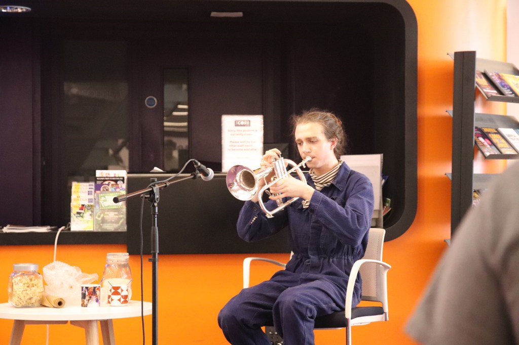 photo of isaac playing flugelhorn into a microphone, next to a table of domestic food items